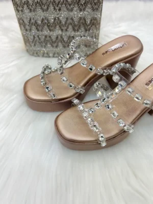 Elevate your festive look with our Cinderella Crystal Platform Wedges. Featuring trendy transparent straps encrusted with shimmering baguette crystals and a luxurious rose-gold metallic base, these platforms offer high-octane glamour without compromising on stability. Perfect for the modern bridesmaid or a night out.